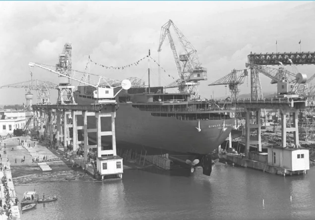 Black-and-white photograph of a ship in a construction berth surrounded by shipyard cranes